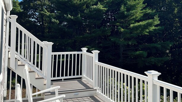 Une terrasse en bois avec des rampes blanches, quelques chaises longues et une vue sur une forêt dense.