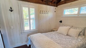 Une chambre avec un plafond en bois, un lit avec une literie à motifs, un ventilateur de plafond et une fenêtre avec des stores.