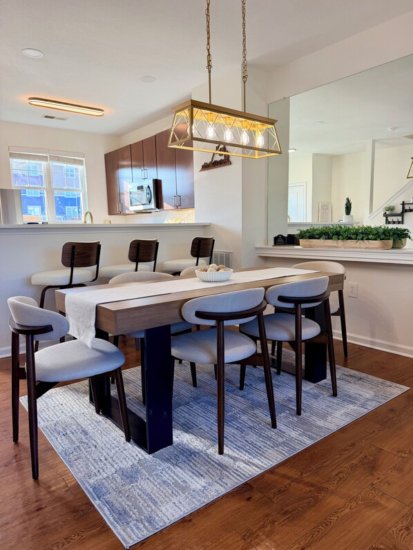 Cocina moderna con comedor, que incluye una gran mesa de madera, seis sillas y una lámpara colgante.