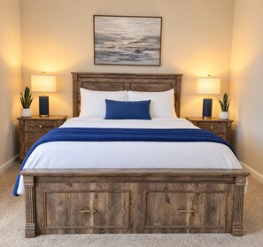 Una cama con cabecera de madera, dos mesitas de noche con lámparas, un cuadro sobre la cama y suelo cubierto de alfombra.