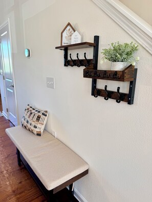 A bench with a cushion, a wall-mounted coat rack with hooks, and a small shelf with decorative items. - Overlook at Liberty: Sleeps 10, <1 Mile to LU + Campus & Mountain Views (Lynchburg)