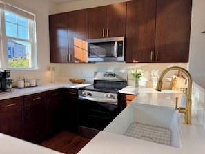 A modern kitchen with dark wood cabinets, a stainless steel microwave, a gas stove, and a white countertop. - Overlook at Liberty: Sleeps 10, <1 Mile to LU + Campus & Mountain Views (Lynchburg)
