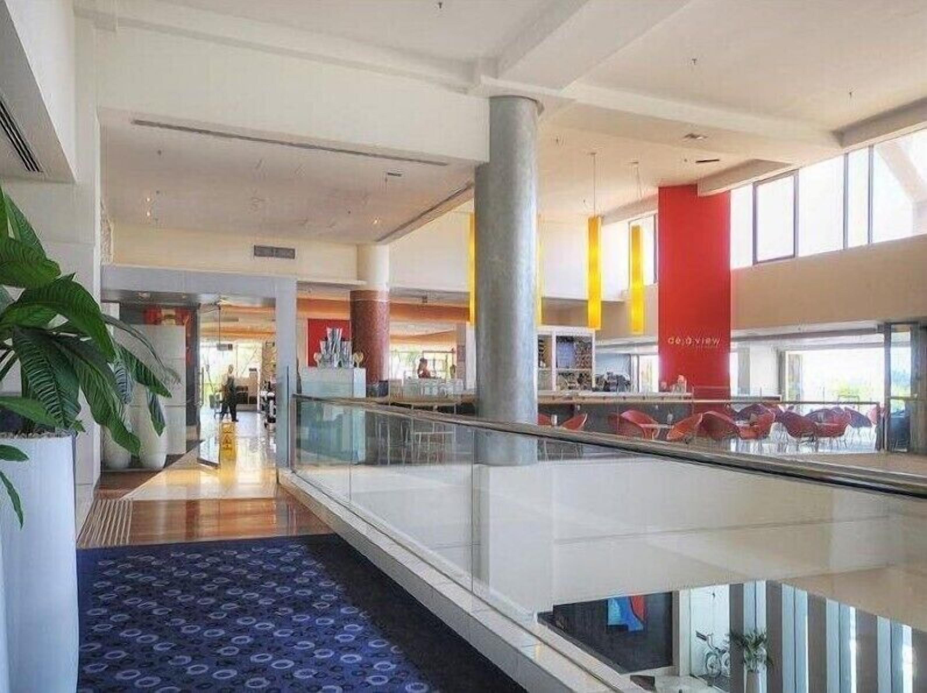 Un moderno hall de hotel con barandilla de cristal, una columna central y una alfombra estampada.