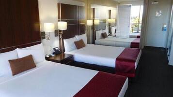 A hotel room with three beds, each with a pillow and a bedside table with a lamp.