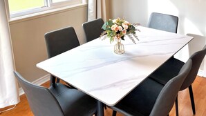 Un coin repas avec une table blanche, des chaises noires, un lustre et un tableau au mur.