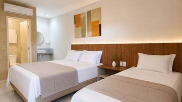 A hotel room with two beds, a wooden headboard, a bedside table, a mirror, and a wall-mounted air conditioner.