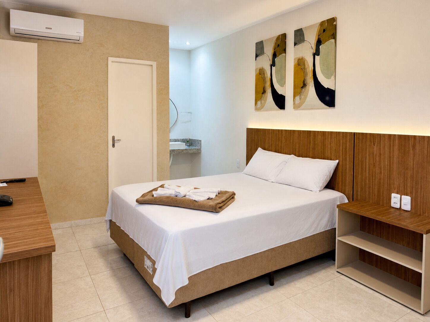 A hotel room with a bed, bedside table, and a wall-mounted air conditioner.
