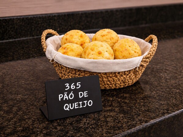 A basket of pão de queijo on a countertop with a sign indicating the price. - Exclusive Hotel (Campos Sales)