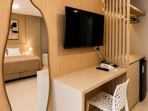 Ett hotellrum med en säng, ett skrivbord med en stol, en tv och en spegel.