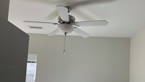 Ein Schlafzimmer mit einem Bett, einem Deckenventilator, einem Fenster und einer Tür.