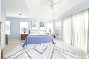Una camera da letto con un letto, due comodini, una ventola a soffitto e ampie finestre con tende.