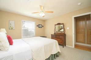 Une chambre à coucher comprenant un lit, une commode, un miroir, un ventilateur de plafond et une porte.
