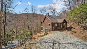 A wooden cabin with a gravel driveway and a fenced area. - Family-Friendly Blowing Rock Retreat | Fire Pit, Game Room, & Cozy Mountain Views (Lenoir)