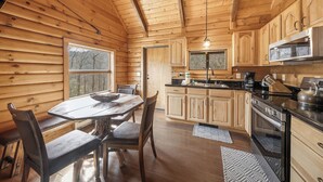 A wooden cabin interior with a dining table, chairs, a kitchen with wooden cabinets, a stove, and a hanging light fixture. - Family-Friendly Blowing Rock Retreat | Fire Pit, Game Room, & Cozy Mountain Views (Lenoir)