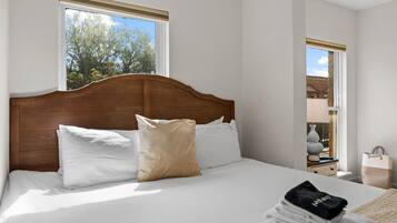 A neatly made bed with white and beige pillows, a wooden headboard, and a window with a view of trees.