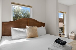 A neatly made bed with white and beige pillows, a wooden headboard, and a window with a view of trees. - Historic Main Street St. Charles - 2BR (Saint Charles)