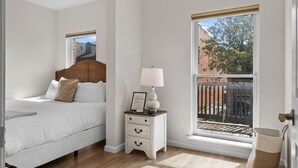 Un dormitorio con cama, mesita de noche, lámpara y vistas al exterior.