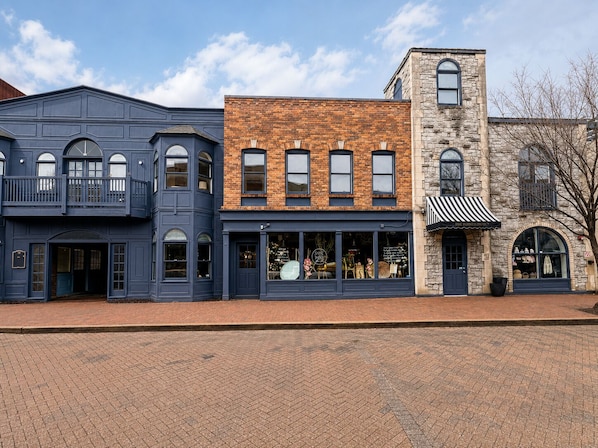 Une rangée d’immeubles à trois étages, dont les façades sont faites d’un mélange de briques et de pierres, avec de grandes fenêtres et une rue pavée de briques.