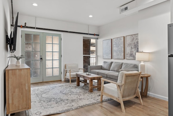 A modern living room with a sofa, coffee table, and a wicker chair. There is a wooden cabinet and a TV mounted on the wall.