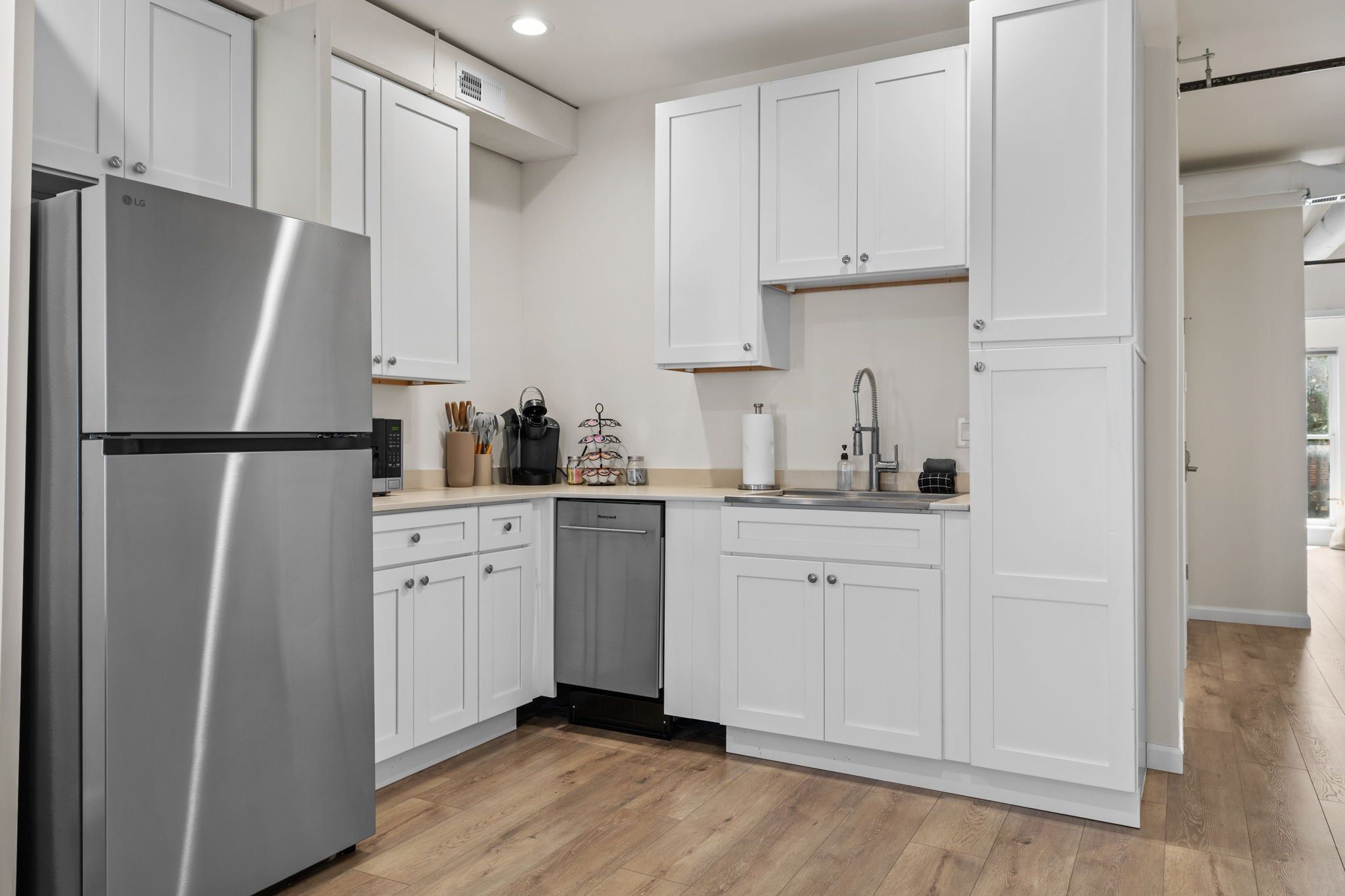 A modern kitchen with white cabinets, stainless steel appliances, and a wooden floor.