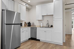 A modern kitchen with white cabinets, stainless steel appliances, and a wooden floor.