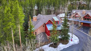 Eine Lodge mit einem Steinkamin, roten und blauen Dächern, umgeben von verschneitem Gelände und dichtem Wald.