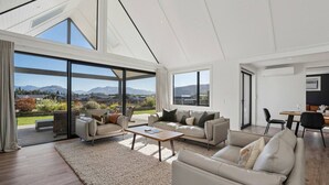A spacious living room with a large window, a sofa set, a coffee table, and a dining area. - Miharo Mountain Haven | Mountain Views & Outdoor Fire (Wānaka)