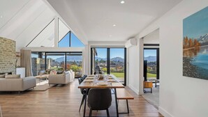 A spacious living area with a dining table, sofas, and a large window offering a mountain view. - Miharo Mountain Haven | Mountain Views & Outdoor Fire (Wānaka)