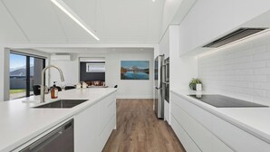 A modern kitchen with white cabinetry, stainless steel appliances, and a wooden floor. - Miharo Mountain Haven | Mountain Views & Outdoor Fire (Wānaka)
