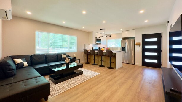 A modern living room with a sofa, coffee table, and a kitchen area with a refrigerator and bar stools. - 3-Bed, 4-Bath Modern Home - Open Concept, Fully Remodeled & Brand-New Furnished (Los Angeles)