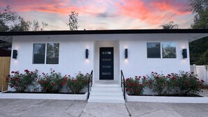 A modern house with a white exterior, a black front door, and red flowers in front. - 3-Bed, 4-Bath Modern Home - Open Concept, Fully Remodeled & Brand-New Furnished (Los Angeles)