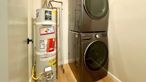 A compact laundry room with a stacked washer and dryer, a water heater, and visible plumbing. - 3-Bed, 4-Bath Modern Home - Open Concept, Fully Remodeled & Brand-New Furnished (Los Angeles)