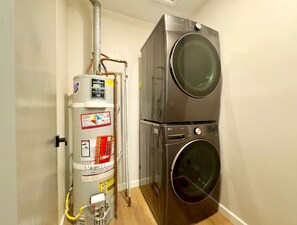 A compact laundry room with a stacked washer and dryer, a water heater, and visible plumbing. - 3-Bed, 4-Bath Modern Home - Open Concept, Fully Remodeled & Brand-New Furnished (Los Angeles)