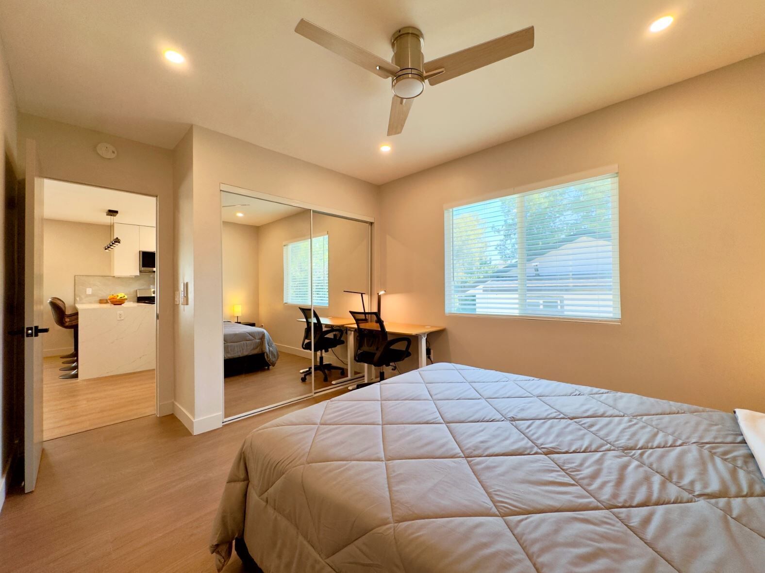 A bedroom with a bed, a desk, a chair, a ceiling fan, and a window.