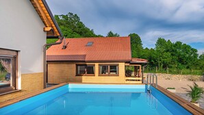 Une maison avec une piscine, une terrasse en bois et un mur en pierre.