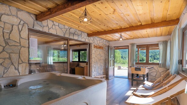 Un espace de bien-être comprenant un jacuzzi, des chaises longues en bois et un mur en pierre.