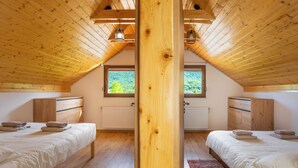 Une chambre avec deux lits, des poutres en bois, une fenêtre et un radiateur.