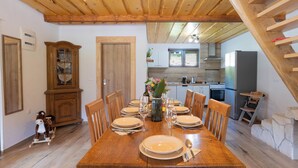 Une salle à manger avec une table en bois dressée pour six personnes, un buffet en bois et une cuisine en arrière-plan.