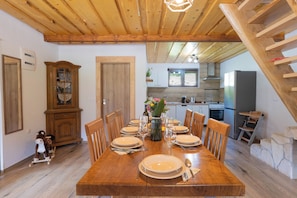 A dining room with a wooden table set for six, a wooden cabinet, and a kitchen in the background. - Relax in Velebit nature with jacuzzi and traditional charm (Gospić)