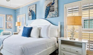 A bedroom with a white bed, a nightstand, a lamp, and wall art. - Beach Paradise by Kaiser • Beachfront w/ Private Access • New Mgmt (Gulf Shores)