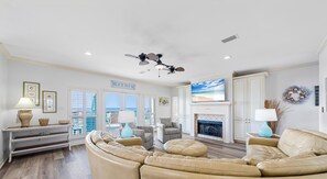 A spacious living room with a fireplace, a ceiling fan, and a large TV screen. - Beach Paradise by Kaiser • Beachfront w/ Private Access • New Mgmt (Gulf Shores)
