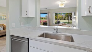 Una cocina moderna con lavavajillas integrado, un lavamanos de acero inoxidable y una ventana con vistas a un jardín.
