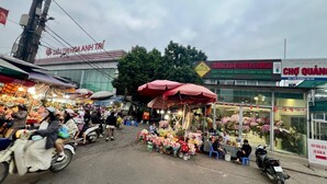 Ein Straßenmarkt mit verschiedenen Ständen, darunter ein Blumenstand und ein weiterer mit dem Schild 'TRUNG XUAN FLOWER & BONSAI'.