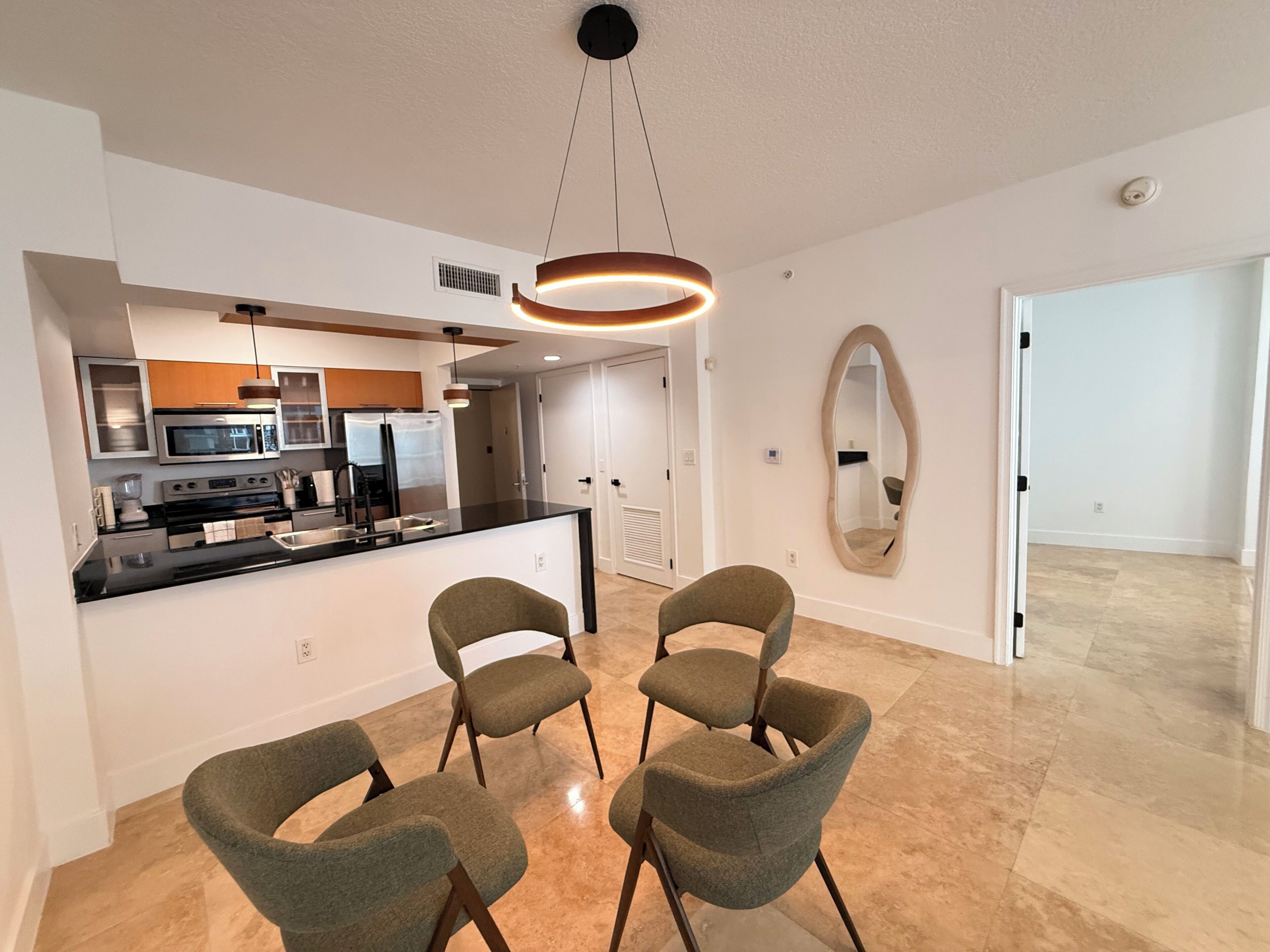 Une cuisine moderne avec un îlot central, un coin repas avec quatre chaises et un grand miroir au mur.