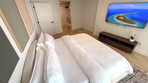 Een slaapkamer met een bed, een televisie waarop een tropisch eiland te zien is, een inloopkast en een gang.