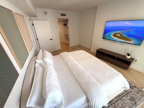 Ein Schlafzimmer mit Bett, Fernseher der eine tropische Insel zeigt, begehbarem Kleiderschrank und einem Gang.