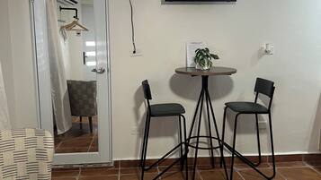 A room with a bed, a TV mounted on the wall, two chairs around a small table, and a door leading to another room.