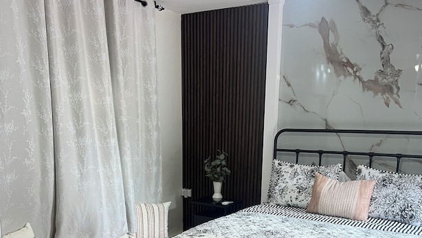 Une chambre à coucher comprenant un lit, une table de chevet, une plante en pot et un mur dont le motif rappelle le marbre.