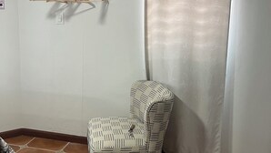 Une pièce comprenant un fauteuil à motifs, un appareil de climatisation, un rideau et un porte-manteau fixé au mur.