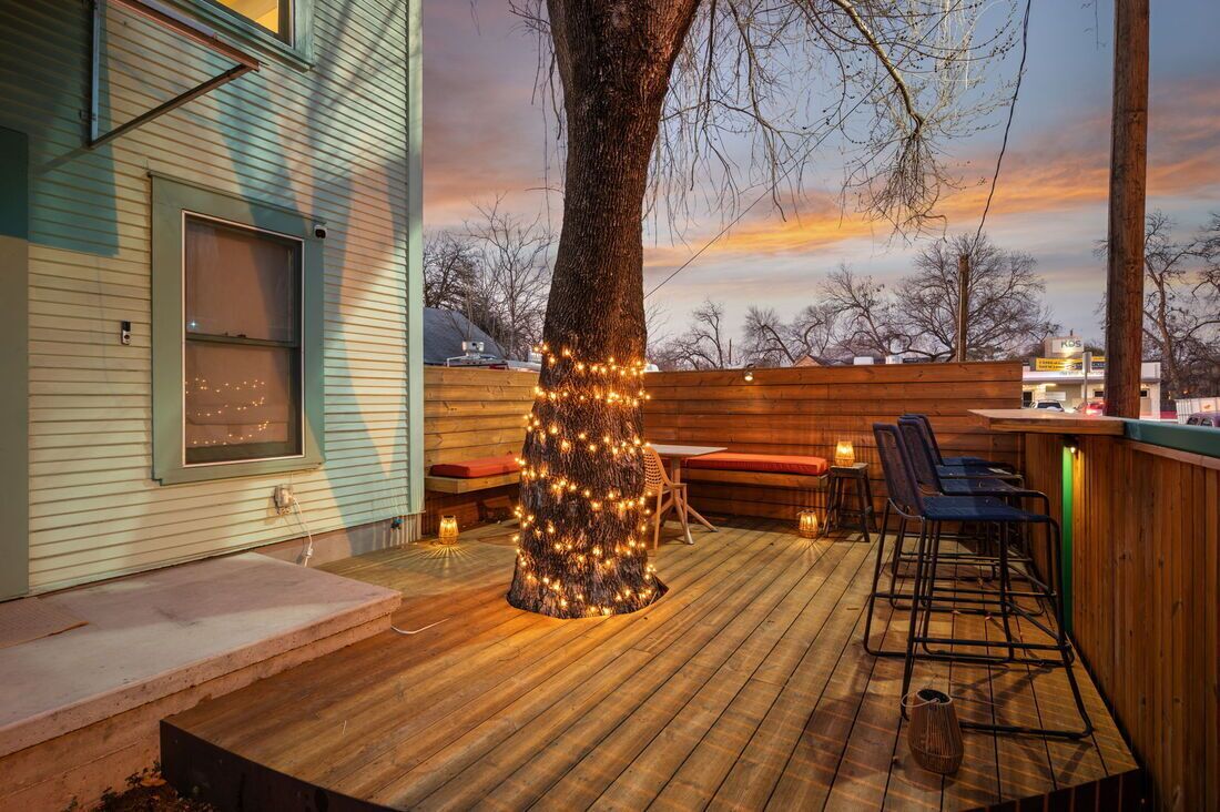 Una terrassa de fusta amb un arbre il·luminat per llums, una zona de bar amb seients i vista del cel.